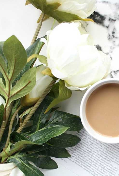 A white flower resting beside a steaming cup of coffee, evoking a sense of calm and relaxation.