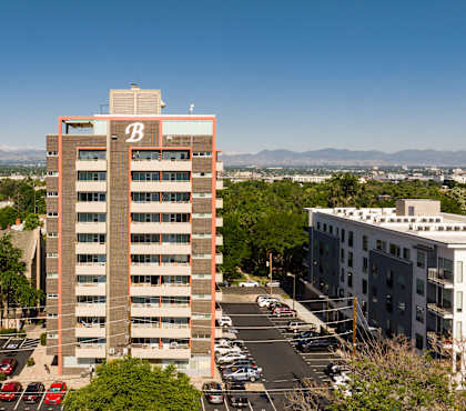 A tall building with the letter B on it is in the middle of a parking lot.