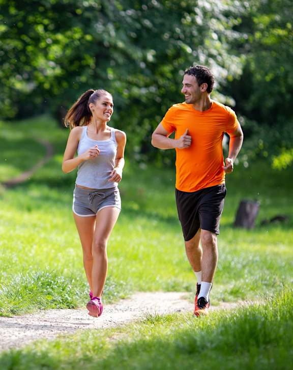 A man and a woman jogging on a path in a green park.