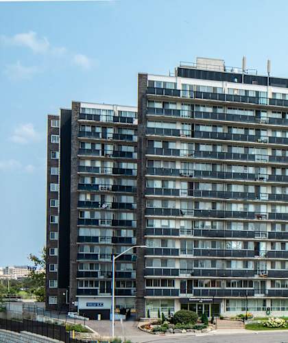 A large, modern building with many windows is surrounded by a grassy area and a road.