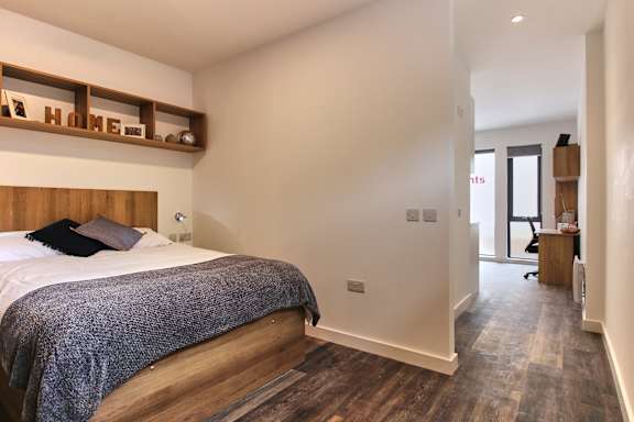A bedroom with a bed, wooden headboard, and a grey blanket.