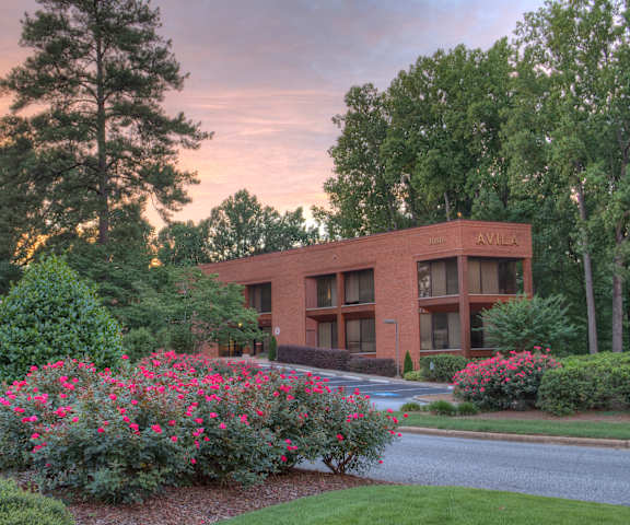 A building with the word "AVILK" on it is surrounded by greenery and flowers.