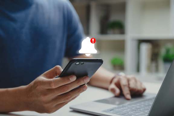 A person holding a smartphone with a red exclamation mark on the screen.