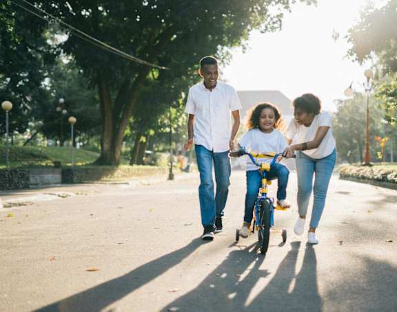 a young girl riding a bike down the street with her family