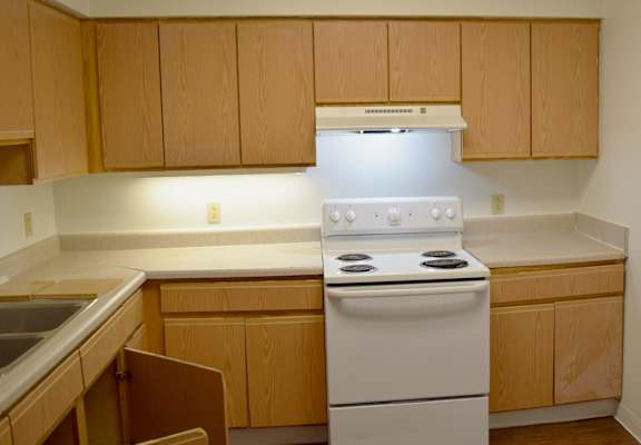 A kitchen with a white stove and wooden cabinets.