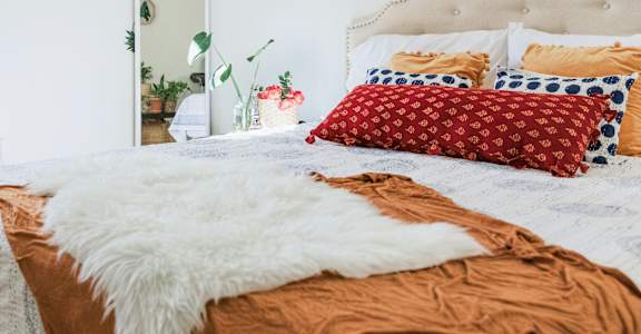 A bed with a white headboard and a white furry throw on it. at Oaks of Westlakes Apartments, San Antonio, 78245