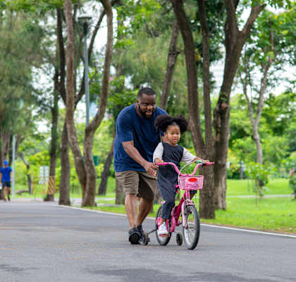 A man and a child are riding a bicycle together on a tree-lined road.