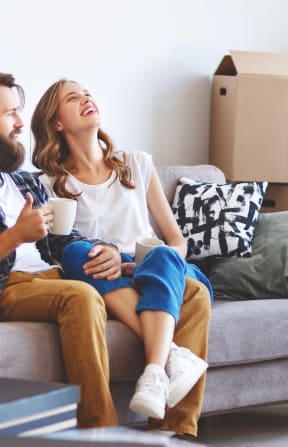 a couple sitting on a couch in a room full of cardboard boxes