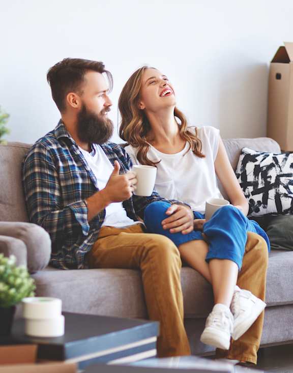a couple sitting on a couch in a room full of cardboard boxes
