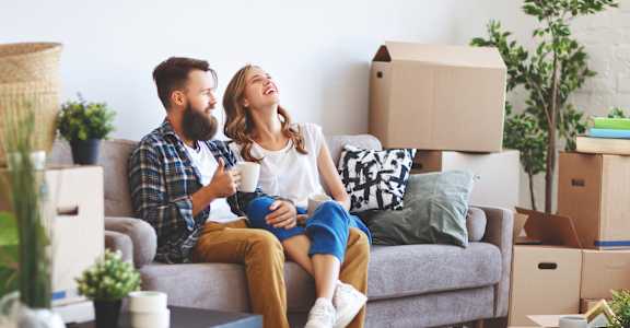 a couple sitting on a couch in a room full of cardboard boxes