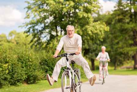 An older man and woman ride bicycles on a path in a park.