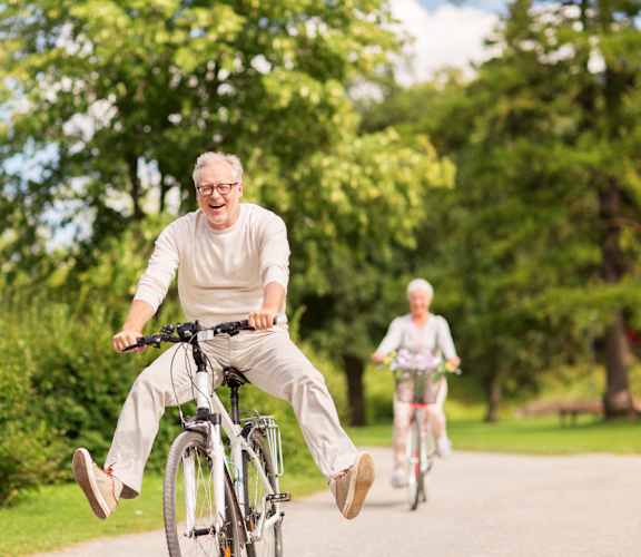 An older man and woman ride bicycles on a path in a park.