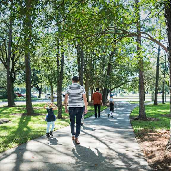 A family of three walks down a tree-lined path.
