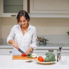 A woman is cutting vegetables on a white countertop at Atlantic Pointe Apartments, Atlantic Highlands