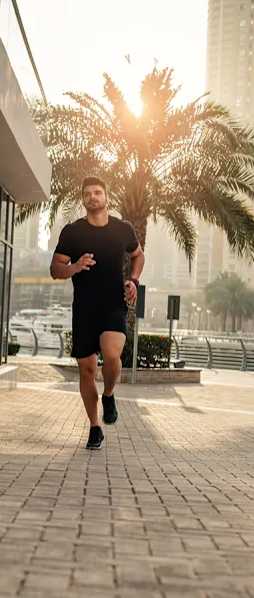 A man is jogging on a paved path with buildings and palm trees in the background.
