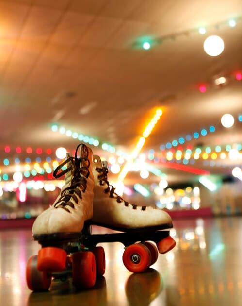 A pair of white roller skates with red wheels.