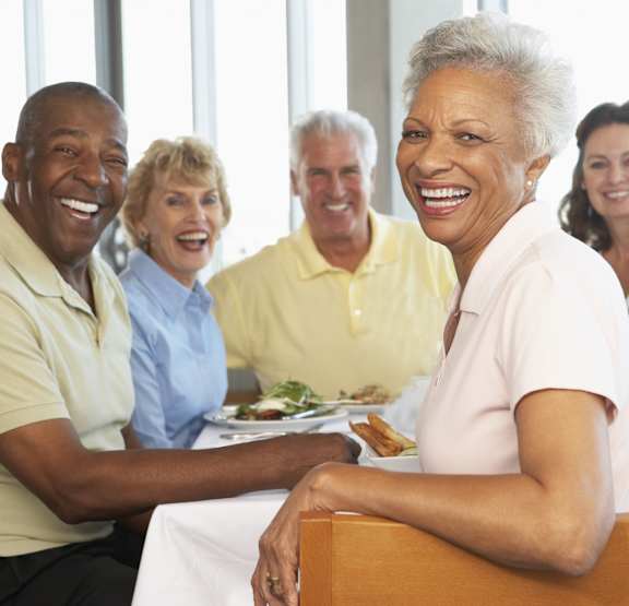 A group of people are sitting around a table smiling.