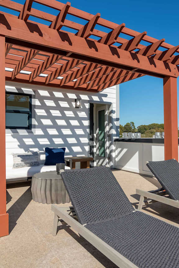 A patio with a pergola and lounge chairs.