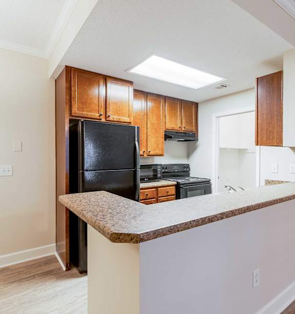 A kitchen with a black refrigerator and brown cabinets at Bedford Parke Apartments, Warner Robins, GA, 31088