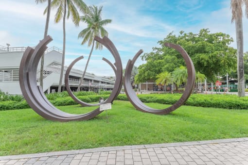 three stainless steel circular sculptures in the middle of a grassy area with palm trees in the