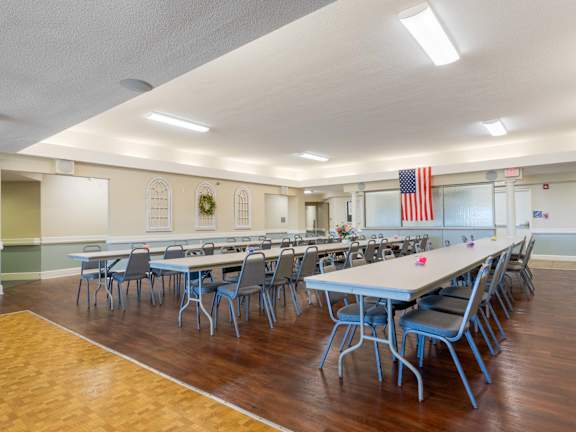 A large room with tables and chairs and an American flag hanging on the wall.