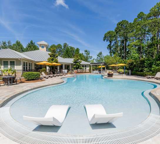 A large swimming pool with white lounge chairs and a house in the background.