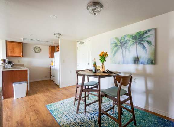 A dining room with a table and chairs and a painting of a palm tree on the wall.