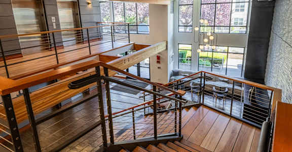 A wooden staircase with metal railings leads to a brightly lit room with a view of the outdoors.