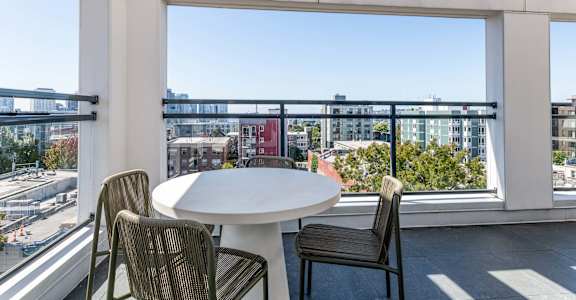 A balcony with a table and chairs overlooking a cityscape.