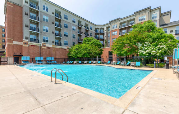 an outdoor swimming pool with chaise lounge chairs and an apartment building in the background