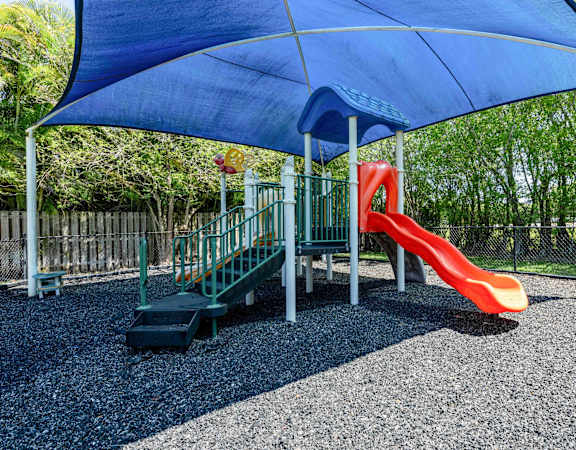 a playground with a slide and a swing set under a blue umbrella