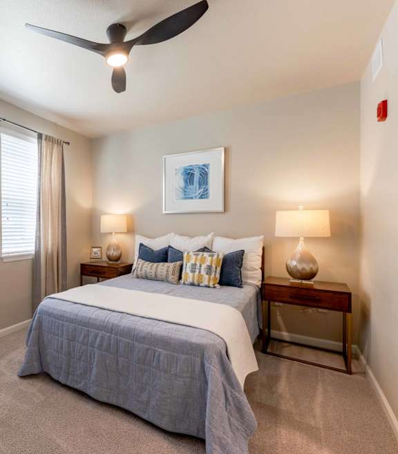 A bedroom with a bed, two lamps, and a ceiling fan.