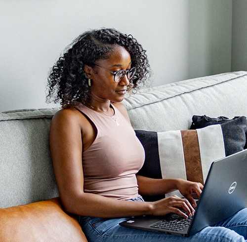 A woman is sitting on a couch using a laptop.