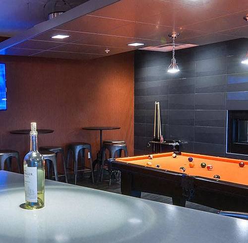 A bottle of wine is on a table in a room with a pool table.