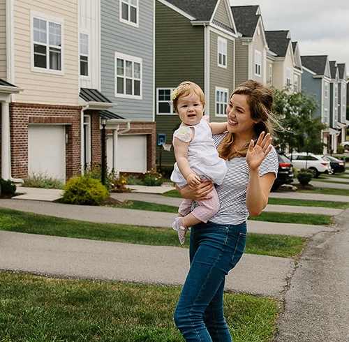 A woman holding a baby is standing on a sidewalk at Highland Village, Pennsylvania
