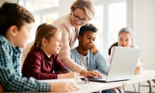 A group of children and an adult are gathered around a laptop, seemingly engaged in a learning activity.