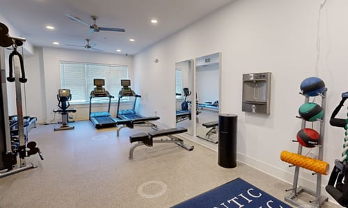 A gym with a variety of equipment including treadmills, weights, and a bench.