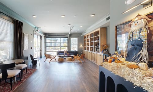 A room with a long table and chairs with a hay bale wall and a scarecrow on the wall.
