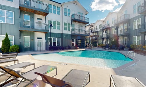 A swimming pool surrounded by lounge chairs and apartment buildings.