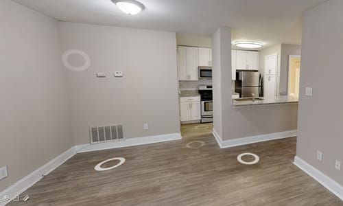 A room with a kitchen in the background and a wooden floor.