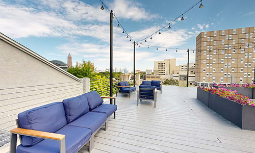 A blue couch is on a wooden deck with a string of lights above it.