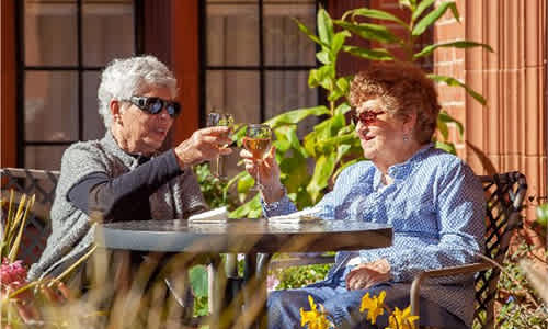 Two women toasting with drinks at an outdoor table.