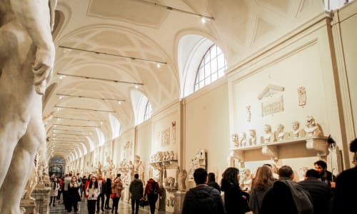 A large room with a high ceiling and a long corridor with a statue on the left.