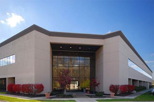 A modern building with a large glass entrance and red bushes in front.
