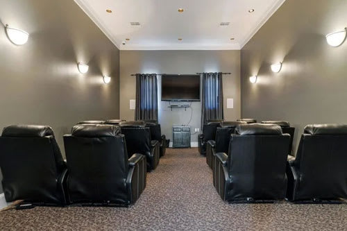 A row of black leather chairs are arranged in a room with a television and curtains.