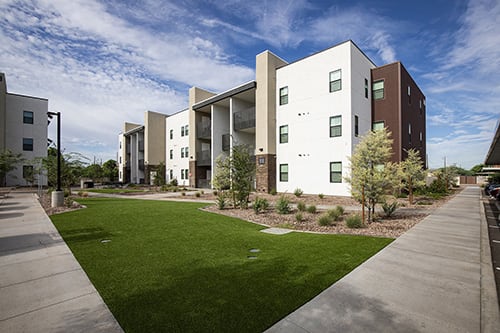 an exterior view of an apartment complex with green grass and a sidewalk