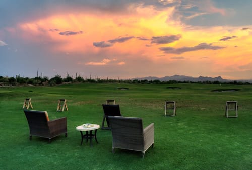 a lawn with chairs and a table and a sunset