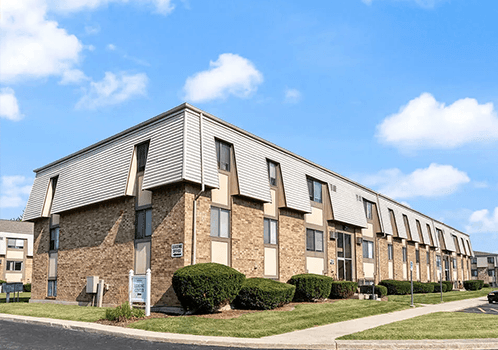 A row of apartment buildings with a blue sky and clouds in the background.