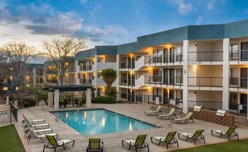 A large apartment complex with a pool and lounge chairs.