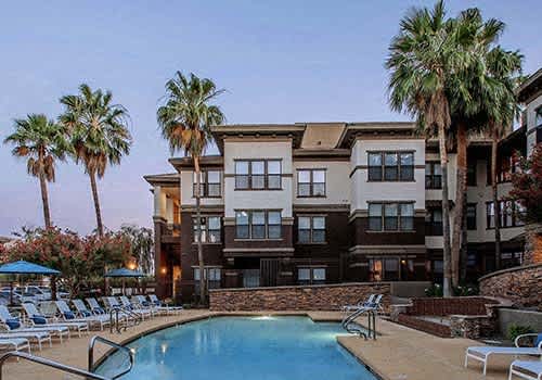 a pool with chairs and palm trees in front of a building